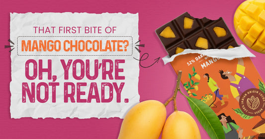 Dark chocolate bar with visible mango pieces partially unwrapped beside whole and sliced mangoes on a pink background, with promotional text reading ‘That first bite of mango chocolate? Oh, you’re not ready